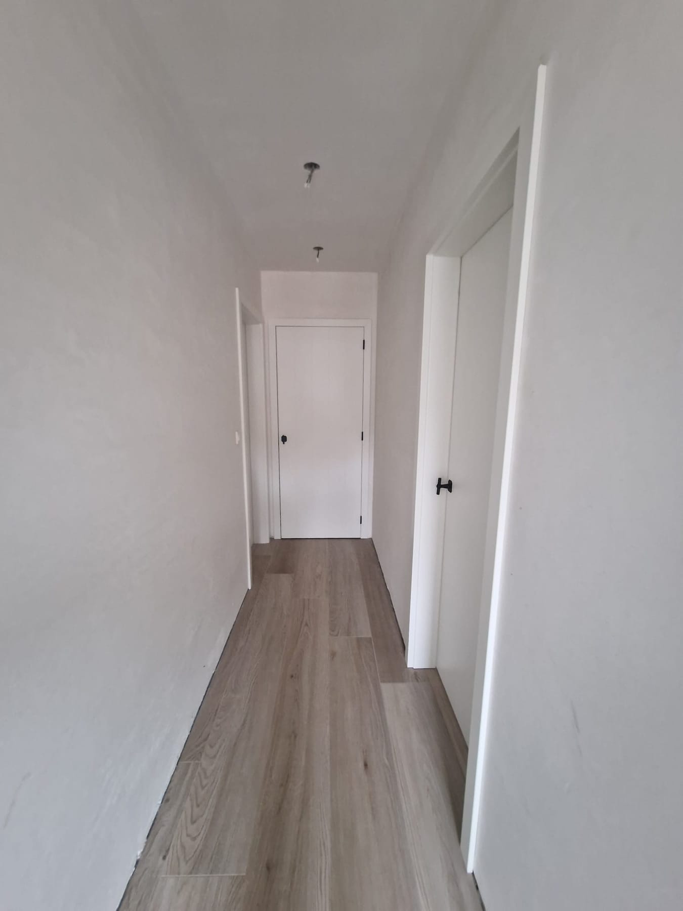 Witte superlak deuren in een gang met houtlook vloer