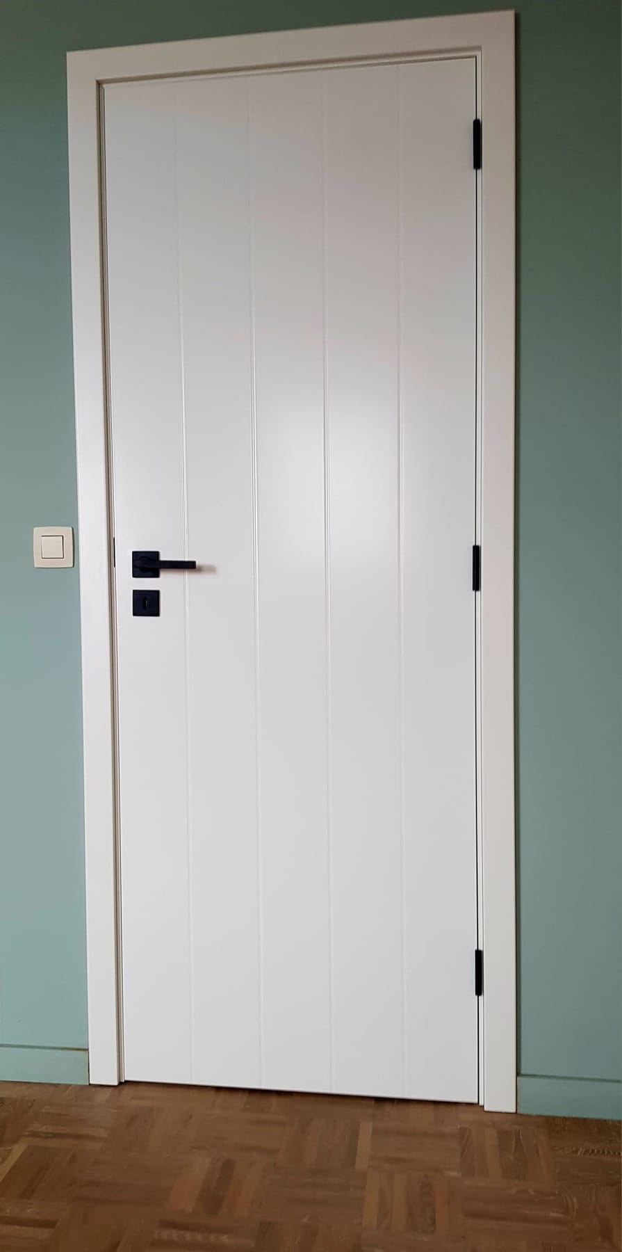 Witte superlak deur met verticale groeven tegen een groene muur